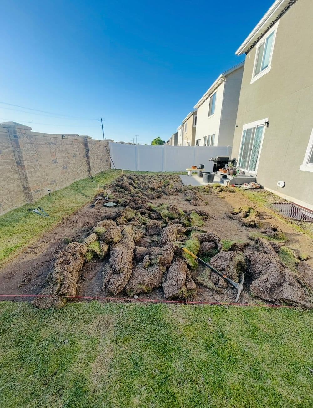 Landscaping project in progress with sod removed and dirt preparation in backyard setting.