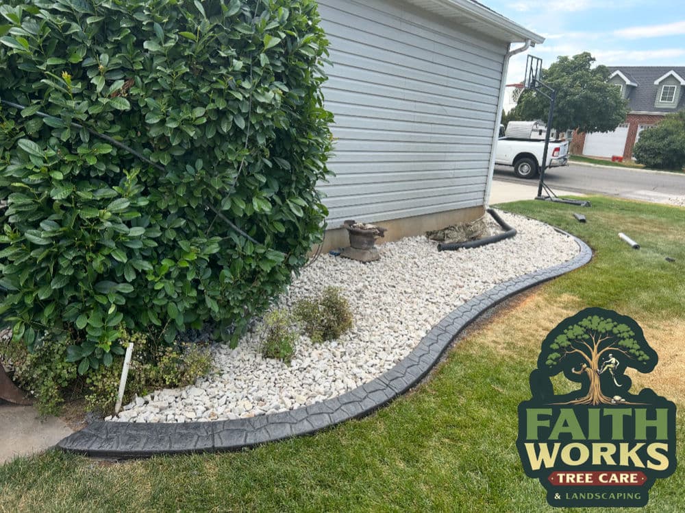 Landscaped yard with gravel, edging, and shrubbery next to a house, featuring Faith Works logo.