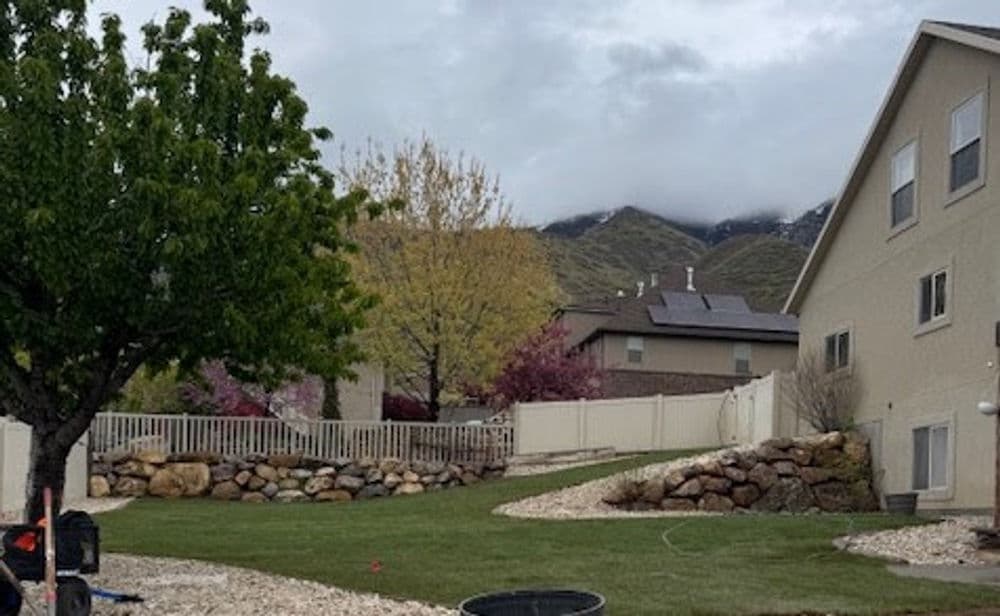 Residential backyard with grass, trees, mountains, and a cloudy sky in the background.