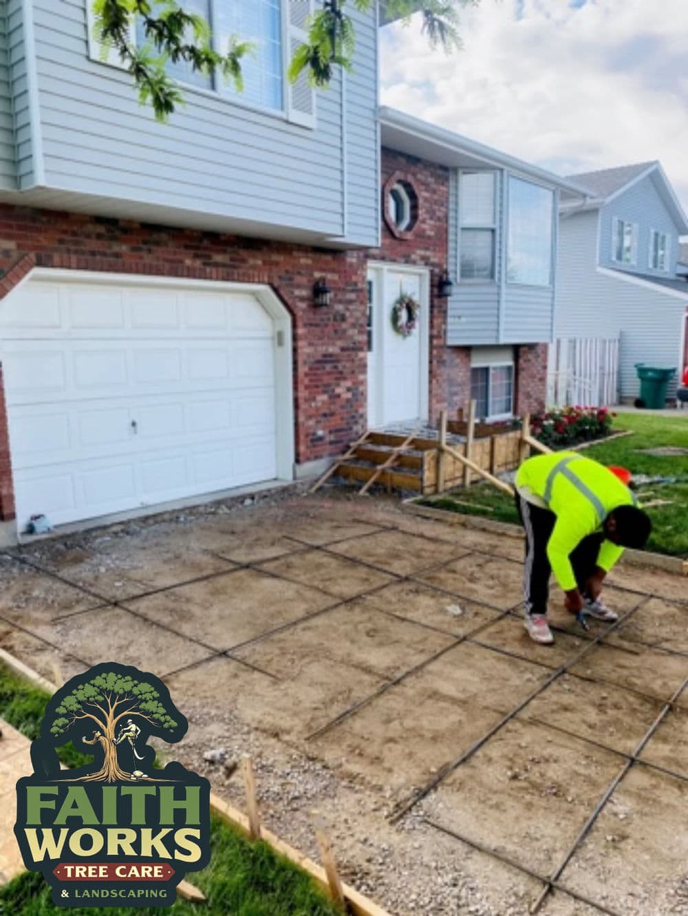 Worker preparing concrete for a walkway at a residence with brick exterior and green landscaping.