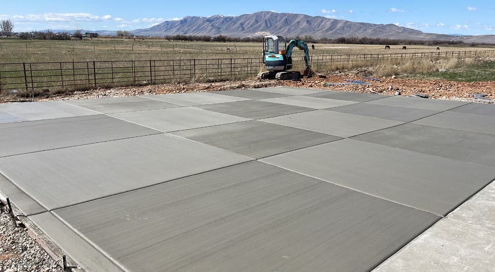 Freshly poured concrete slab on a construction site with machinery and mountains in the background.