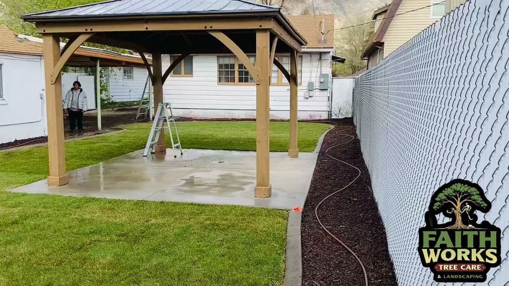 Gazebo in landscaped yard with freshly mowed grass and protective fencing. Faith Works logo visible.