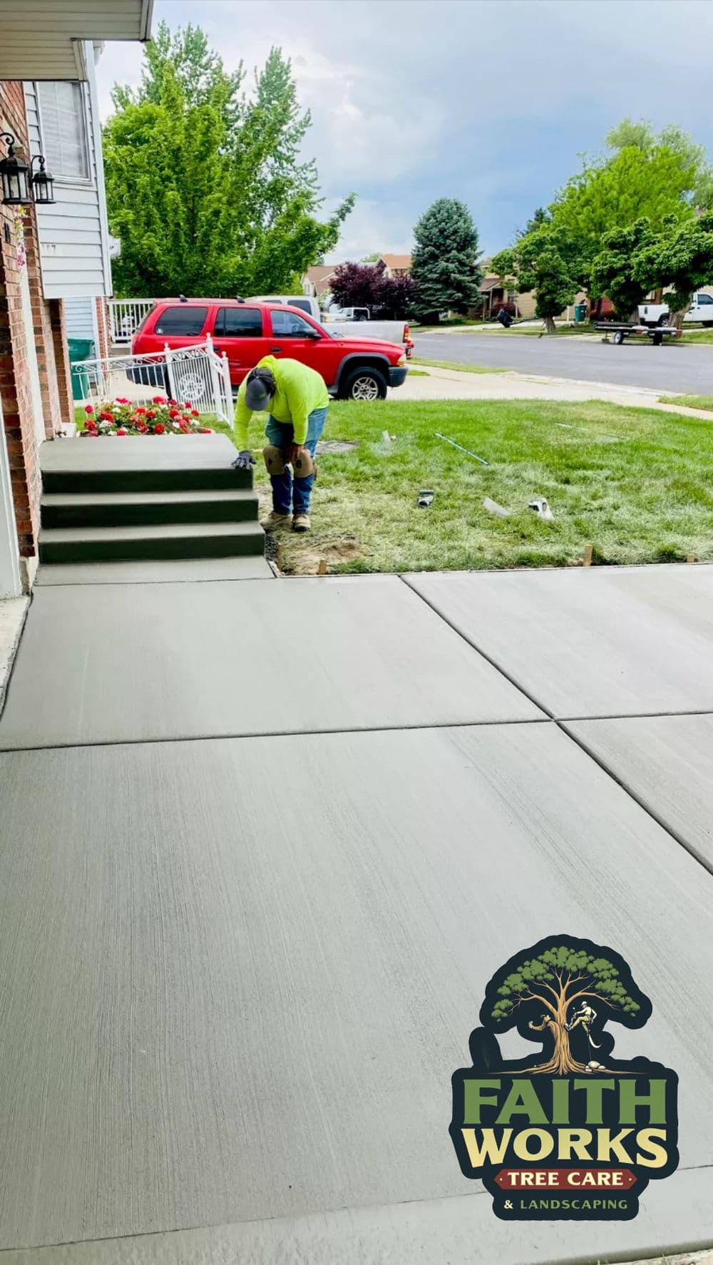 Worker pouring concrete for a new sidewalk installation near landscaped yard. Faith Works logo.