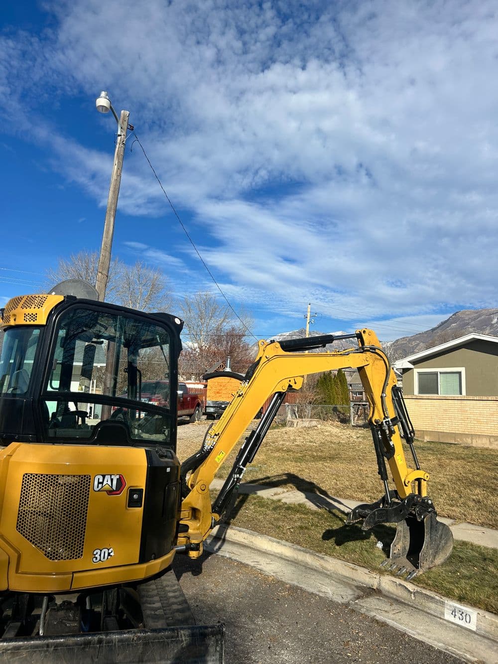 CAT 304 excavator with backhoe attachment parked on residential street under blue sky.