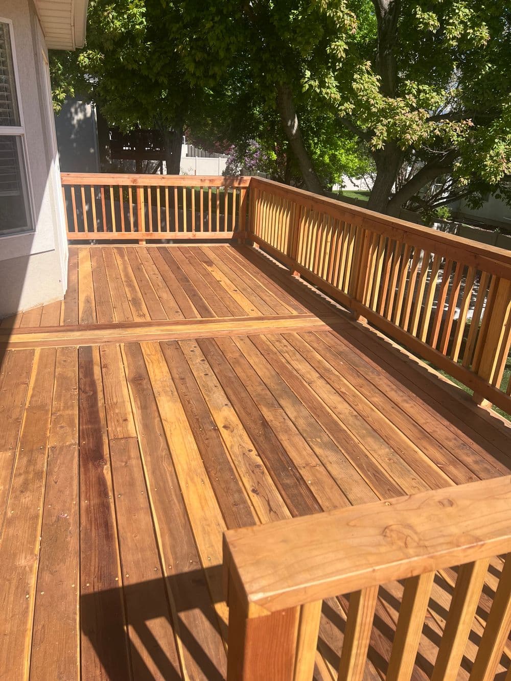 Newly built wooden deck with polished railings and lush green trees in the background.