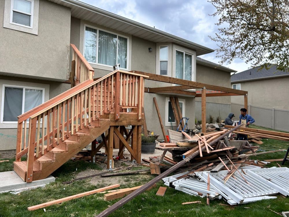 Home renovation: wooden deck under construction with workers and materials in a backyard.