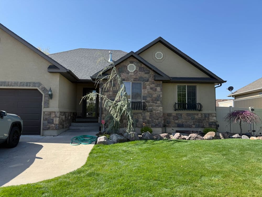 Front view of a cozy stone-accented house with a green lawn and clear blue sky.
