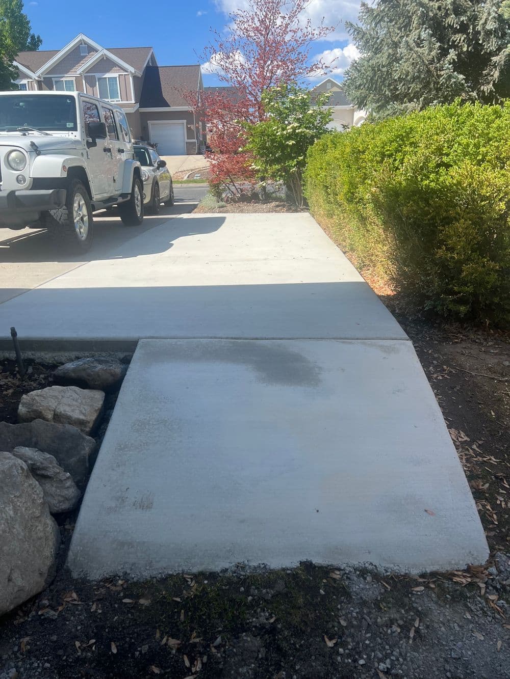 Newly poured concrete driveway with a Jeep parked beside lush greenery and a residential backdrop.