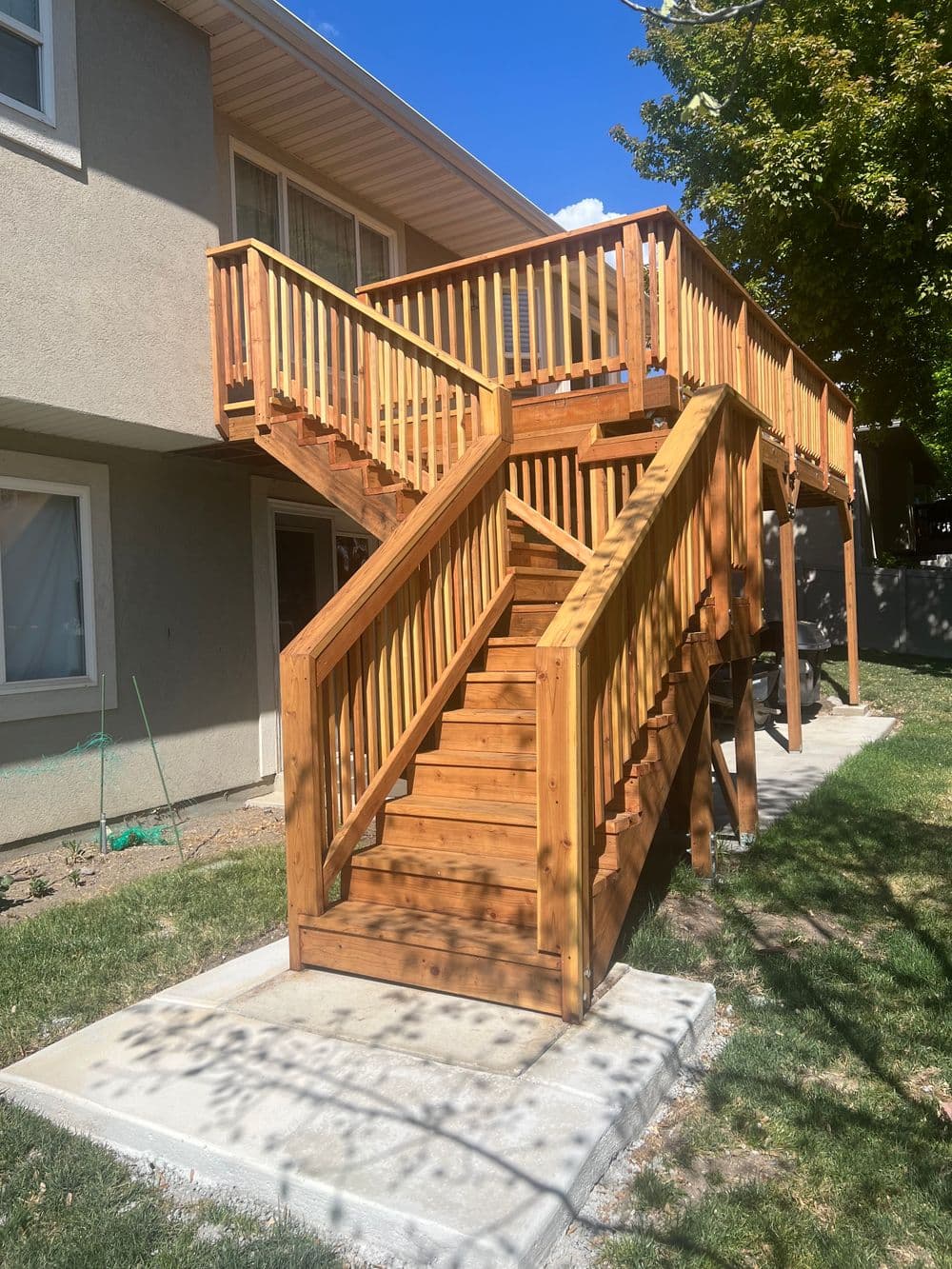 Wooden outdoor staircase with railings, connecting multiple levels beside a residential home.