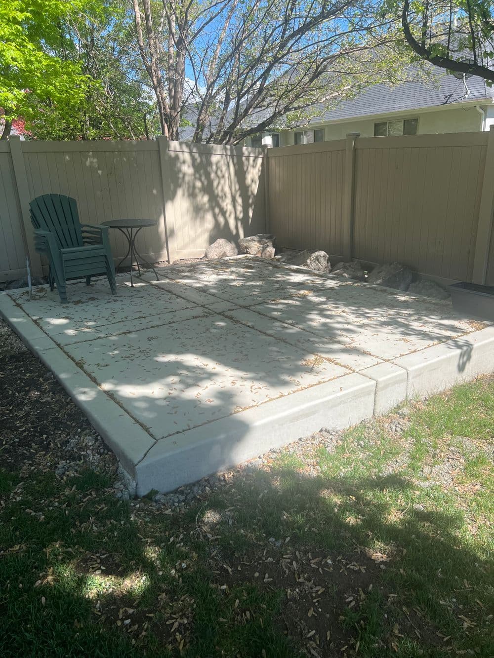 Patio with concrete blocks, green chair, table, and shaded area surrounded by trees.