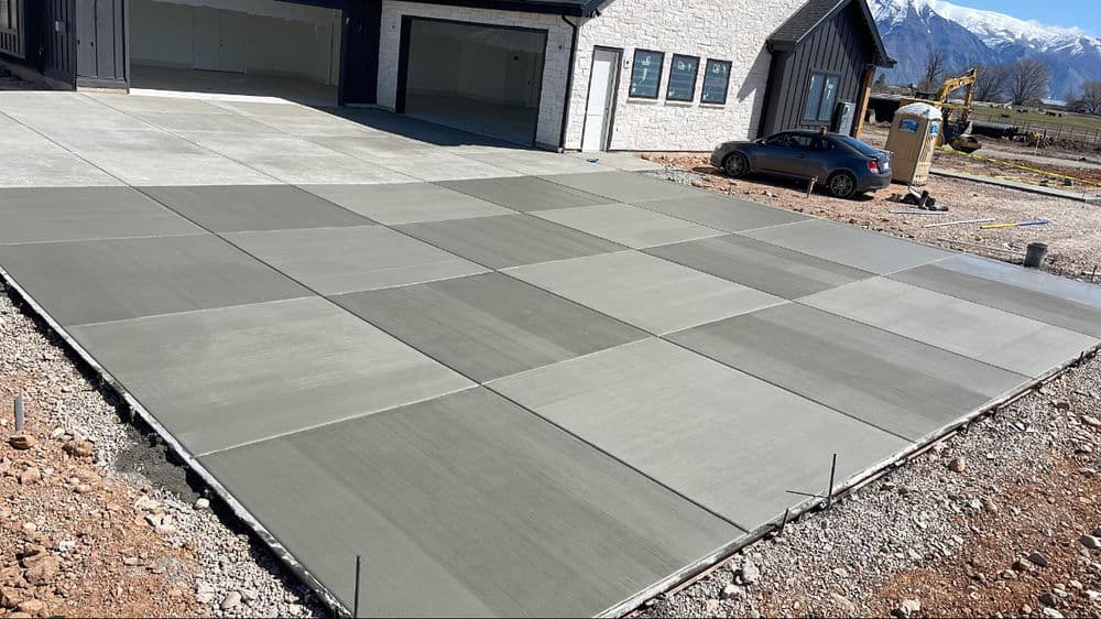 Newly poured concrete driveway with geometric patterns, modern home in the background, scenic mountains.