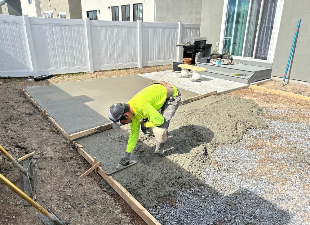 Worker leveling freshly poured concrete in a residential backyard patio construction project.