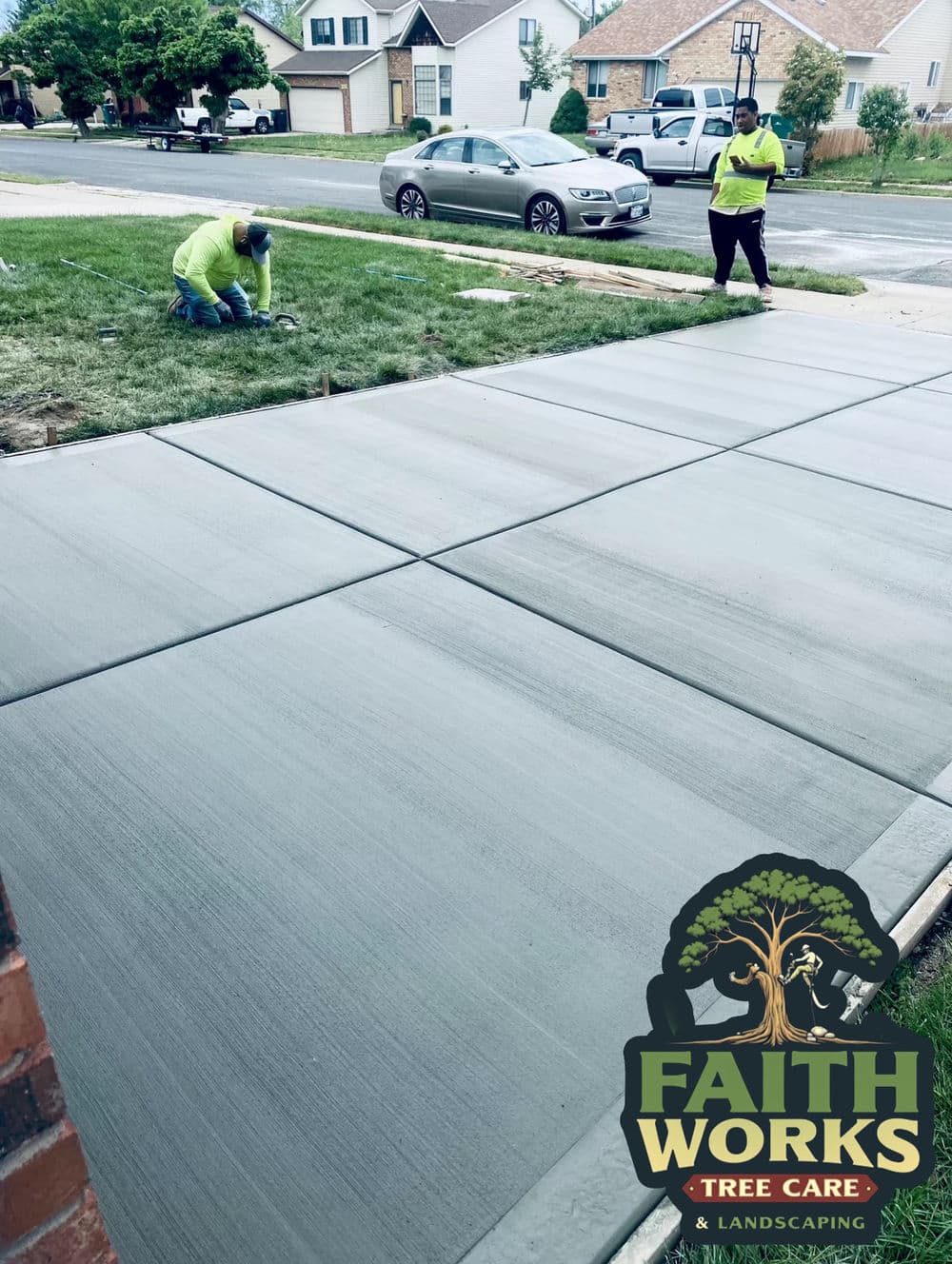 Workers applying fresh concrete on a driveway, showcasing landscaping services by Faith Works.