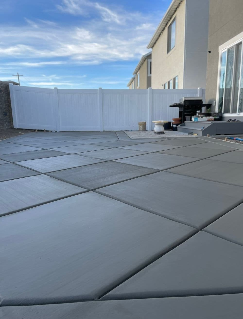 Newly installed gray concrete patio with geometric patterns and a white fence in the background.