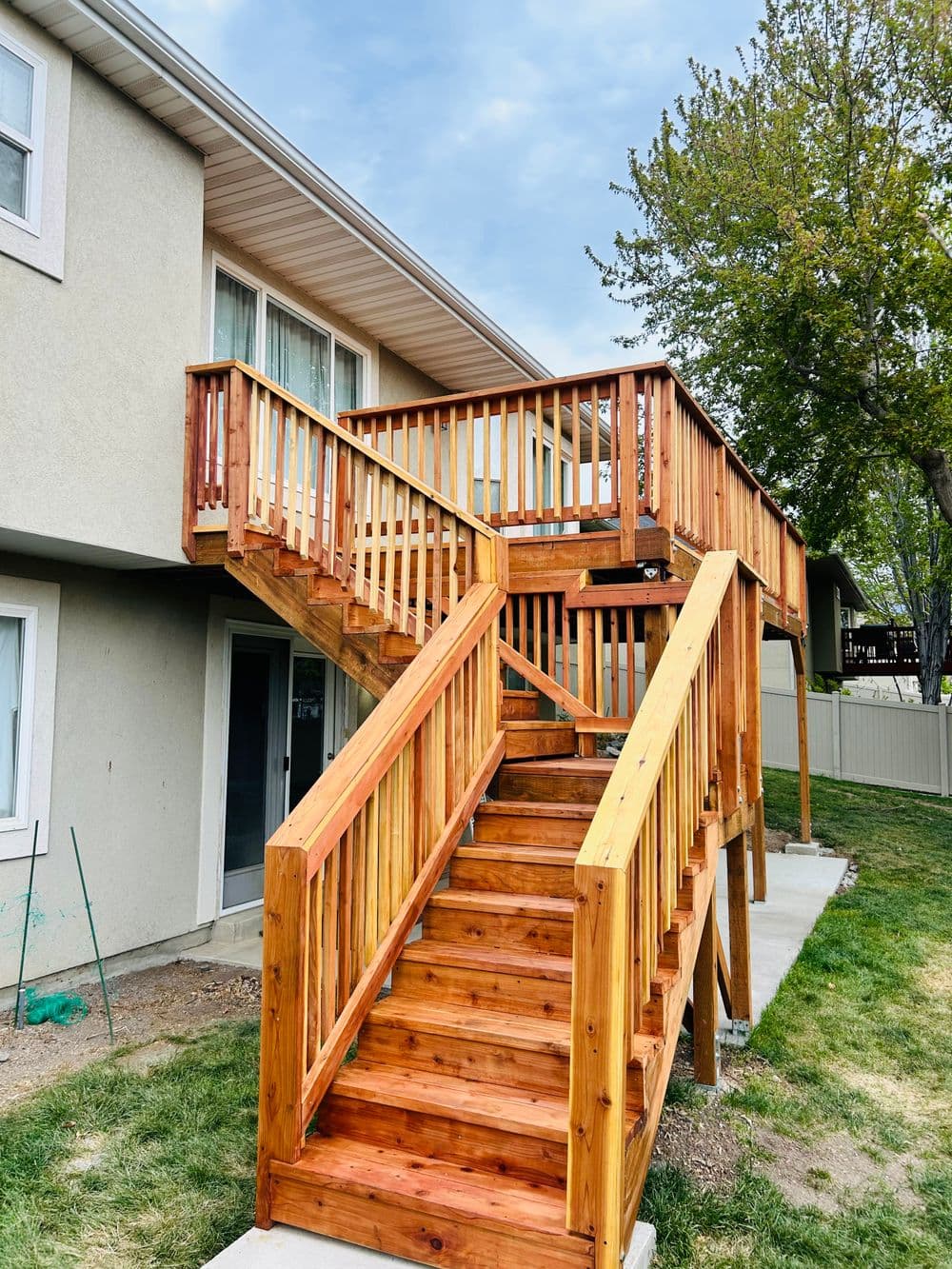 Custom wooden staircase leading to an elevated deck with railings, surrounded by greenery.