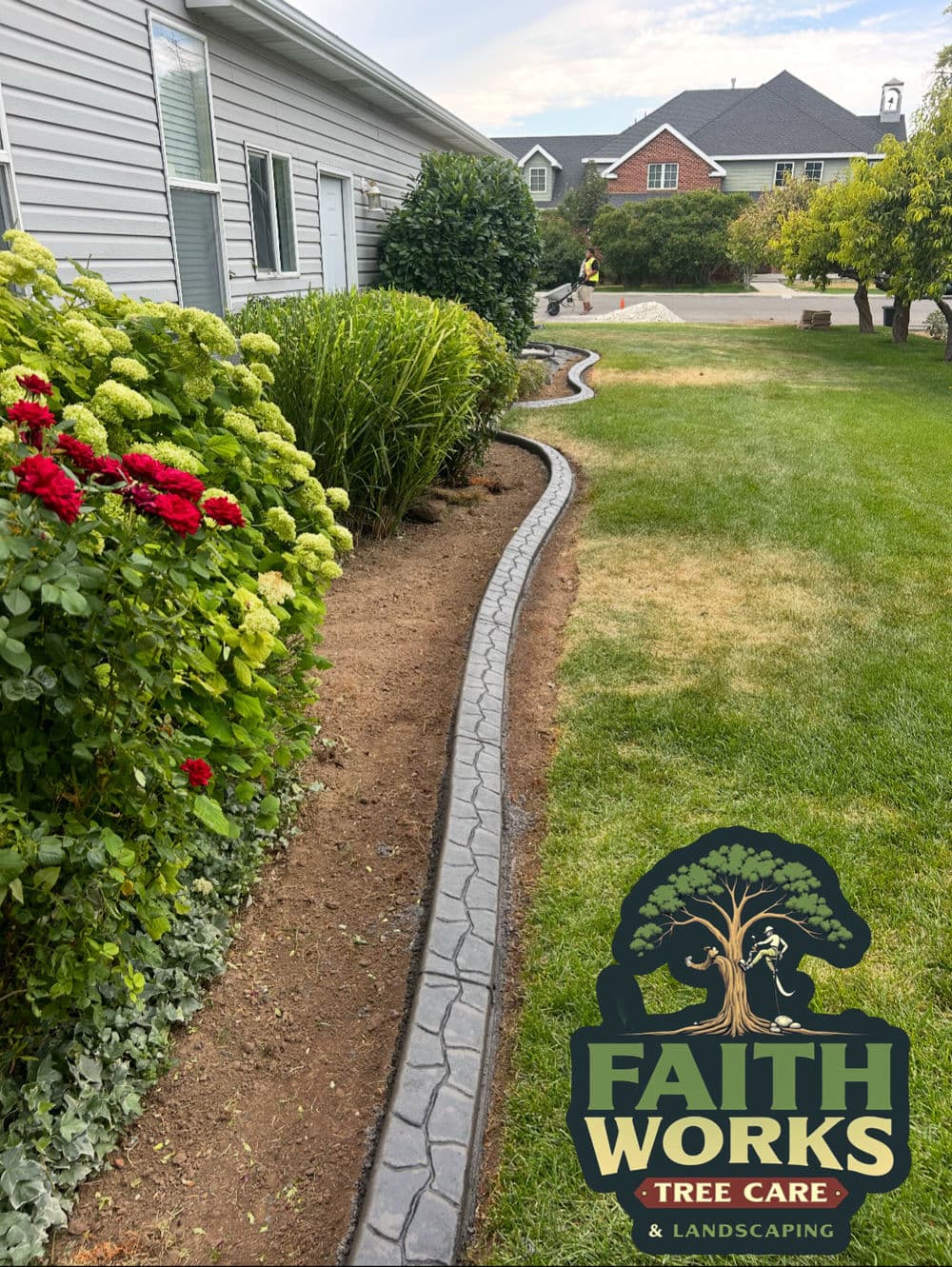 Landscaped garden with a stone border, flowers, and Faith Works Tree Care logo.