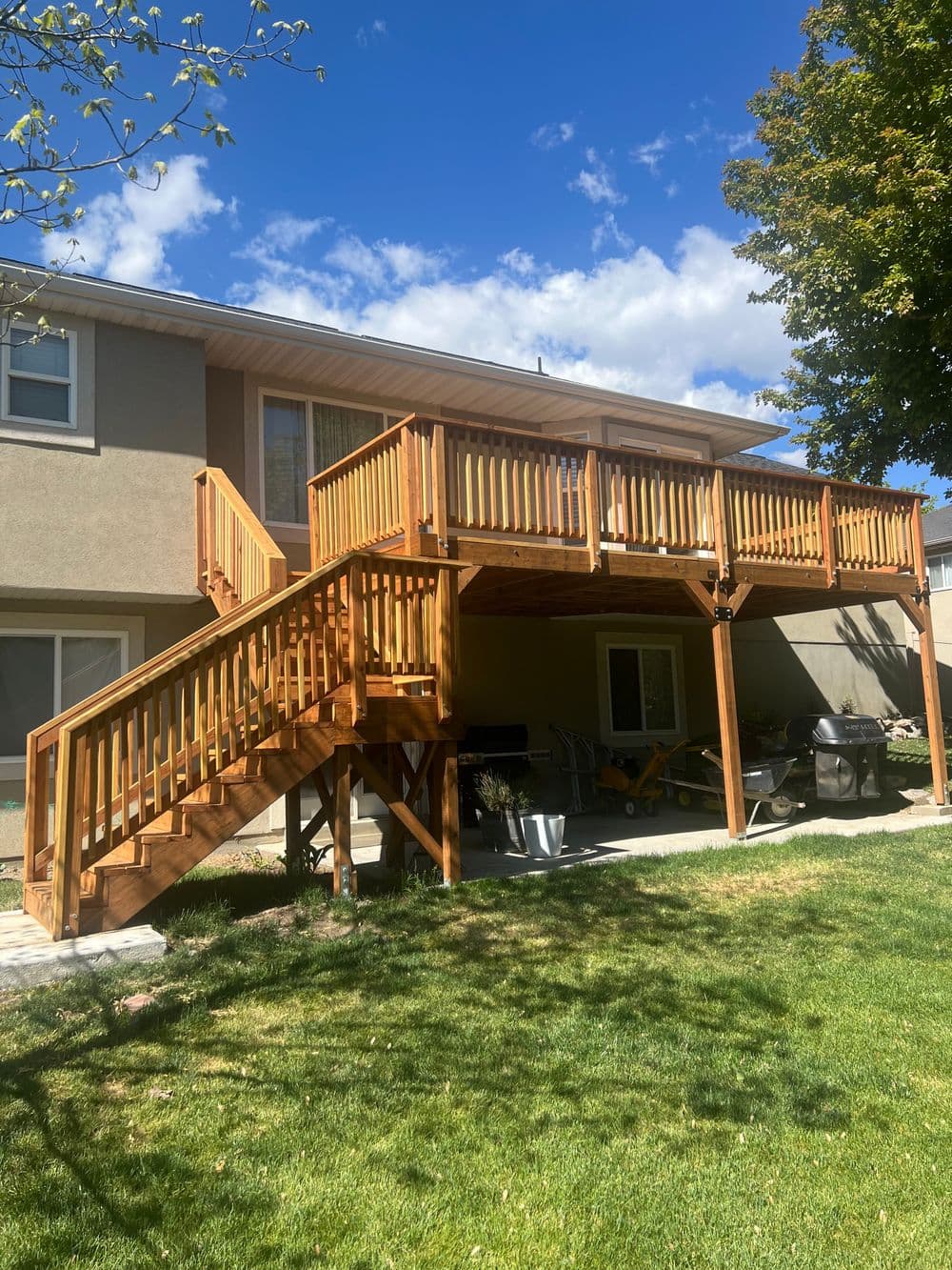 Wooden deck with railings and stairs under a bright blue sky, surrounded by green lawn.